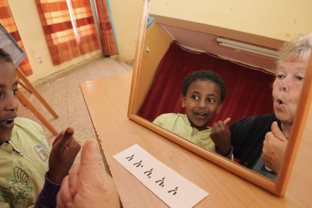 Peili, josta heijastuu iloinen etiopialainen poika. Peilin edessä on lappu, jossa on kirjoitusmerkkejä.