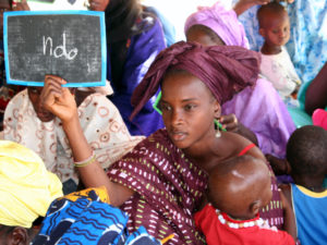 Mauritanialainen nainen opettelee lukemaan lapsi sylissään. Kädessään hänellä on liitutaulu, jossa lukee 