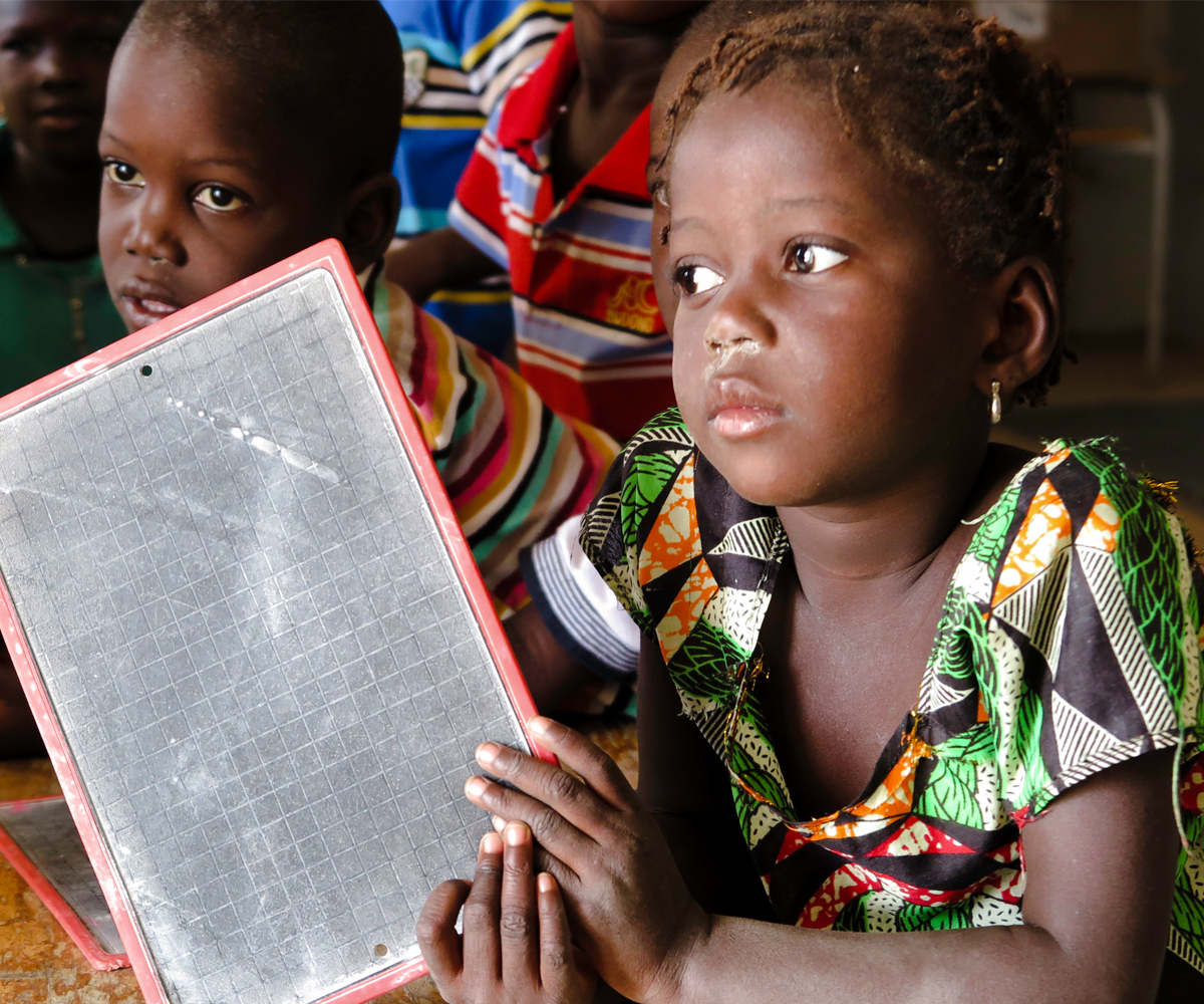 Pikkulapso liitutaulu kädessään lukutaitoluokassa Senegalissa.