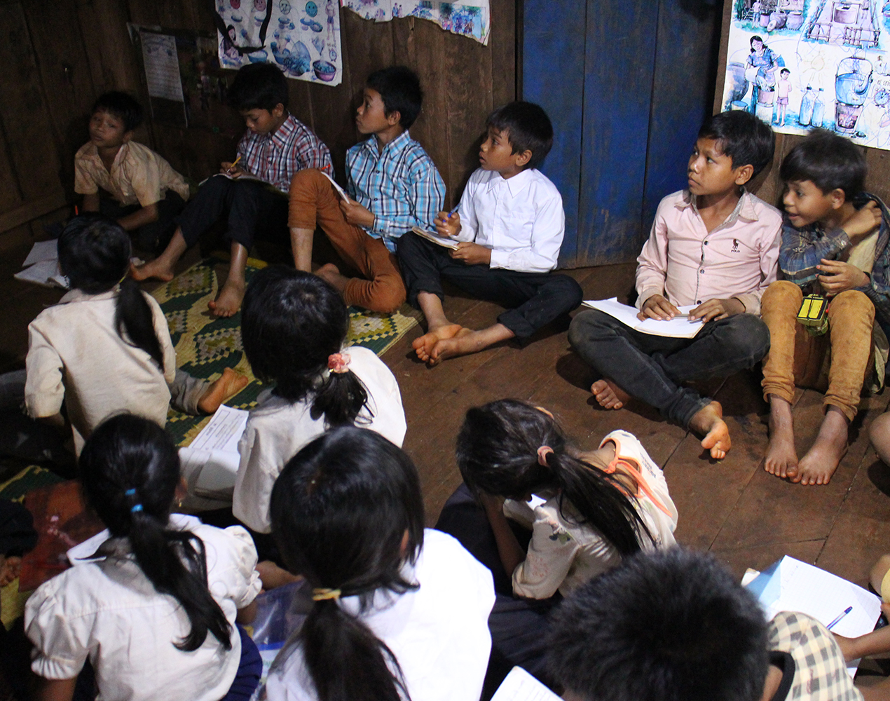 Oppilaita istuu luokan lattialla ja seuraa opetusta