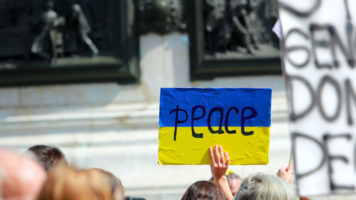Mielenosoittaja pitää ylhäällä Ukrainan lipun värein maalattua kylttiä, jossa lukee Peace.