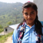7. luokkalainen Manisha hymyilee kameralle koulunsa edessä.