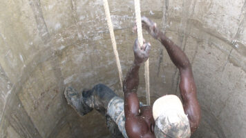 Mies kiipeää köyden avulla kaivosta.