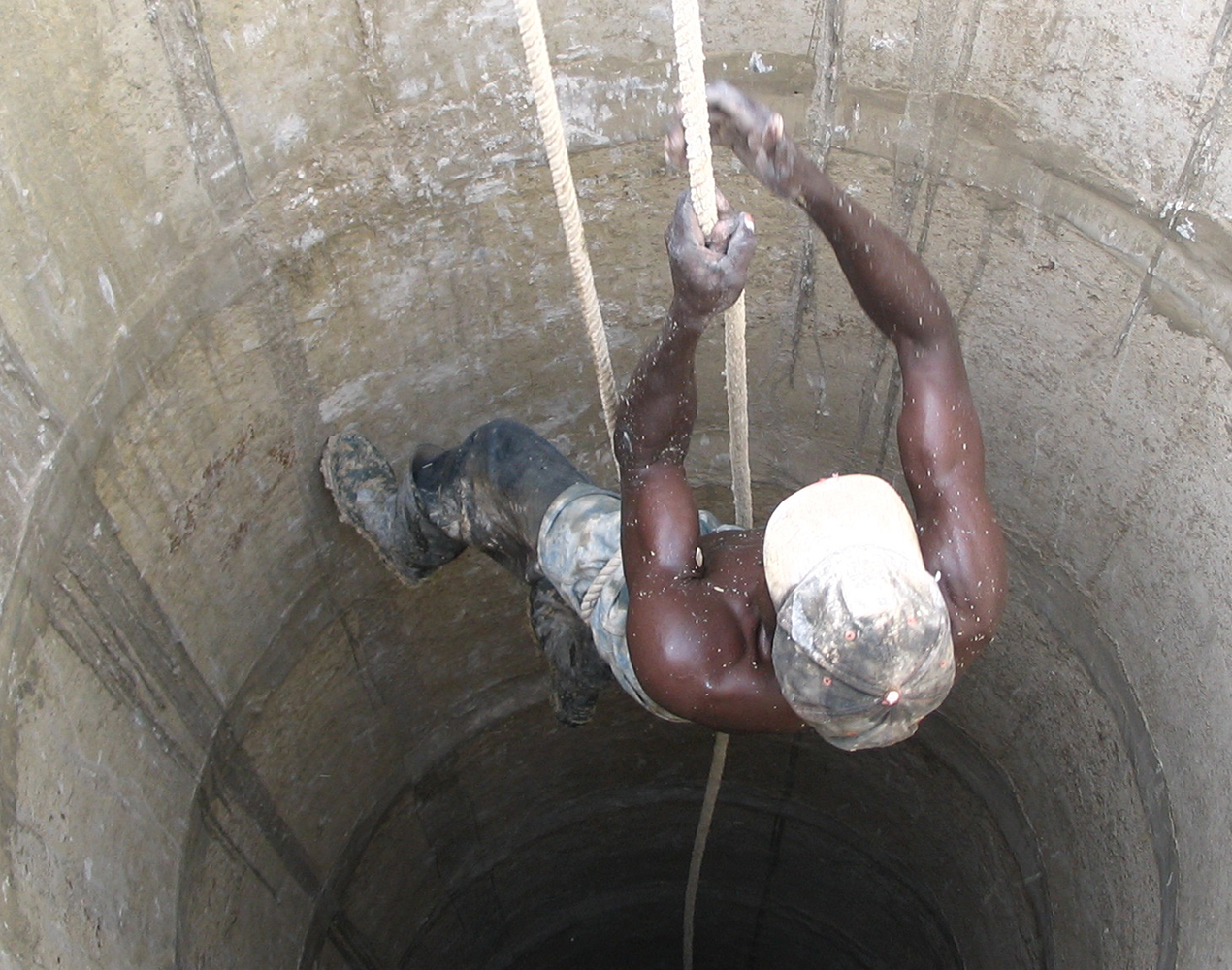 Mies kiipeää köyden avulla kaivosta.