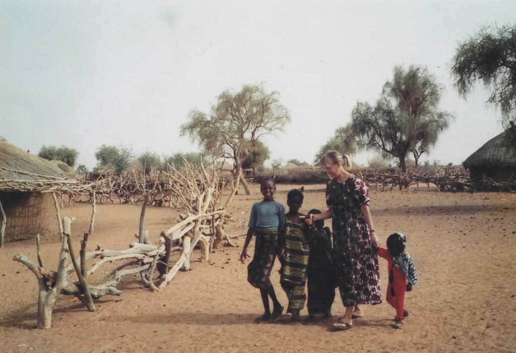 Nainen ja neljä lasta kulkevat käsikkäin senegalilaisessa kylämaisemassa.