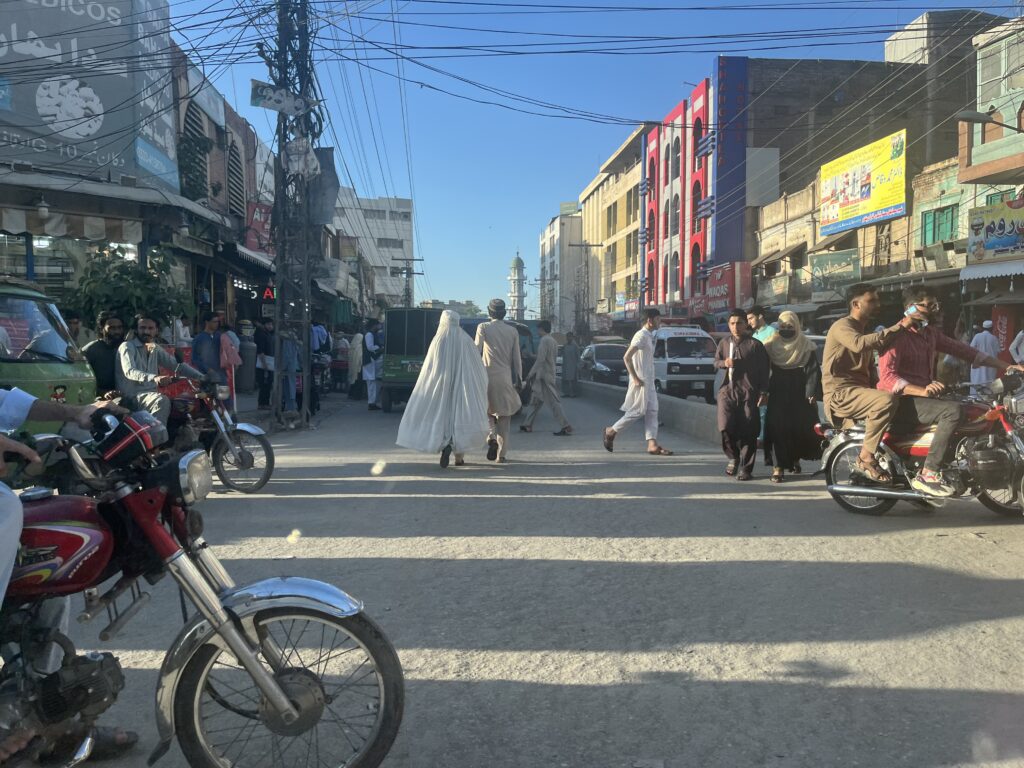 Katukuvaa Peshawarista. Kuvassa näkyy mm. moottoripyöriä sekä käveleviä ihmisiä. Kuvassa näkyvällä naisella on kokonaan peittävä burkha.