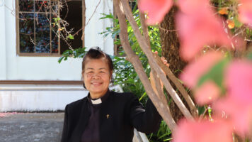 Pastori seisoo kirkon edustalla ja hymyilee kameralle