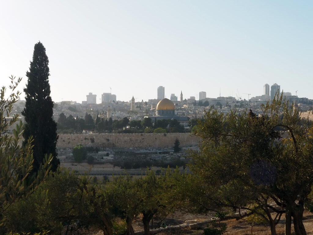 Kuvassa etualalla puita ja taustalla siintää Jerusalemin siluetti jossa näkyy muun muassa kultakupolinen Kalliomoskeija ja vanhaakaupunkia ympäröivä muuri.