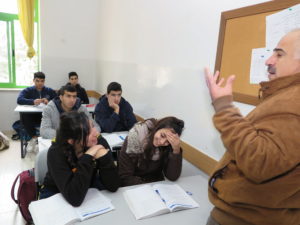Vanhempi miesopettaja opettaa, nuoret palestiinalaiset kuuntelevat.
