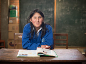 Bolivialainen koulutyttö poseeraa oppikirjan ja pulpetin ääressä koulupuvussaan.