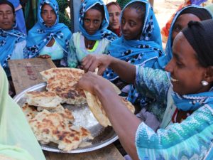 Sinisiin asuihin pukeutuneet etiopialaisnaiset murtavat käsin suurta leipää.