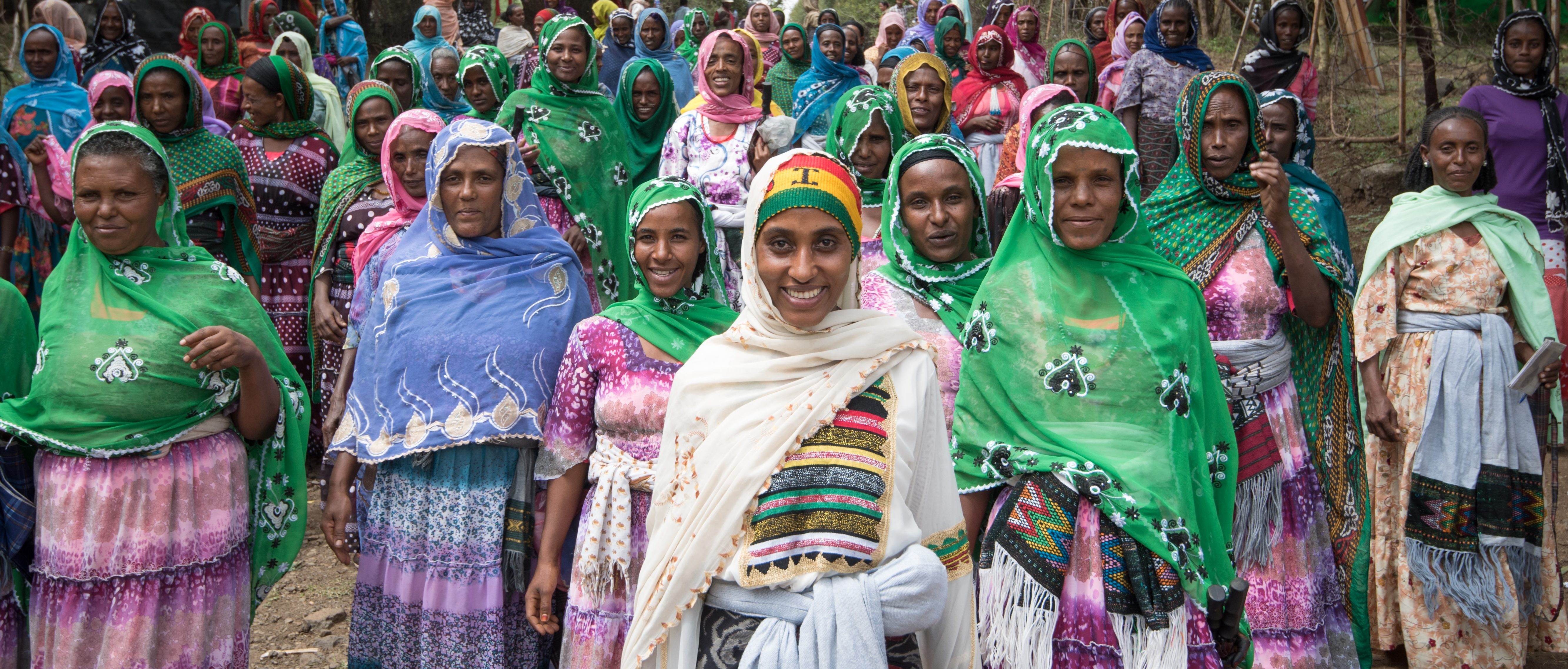 Etiopialaiset iloiset naiset värikkäissä vaatteissaan kulkevat pölyisellä maantiellä. Tiellä on kymmeniä naisia.