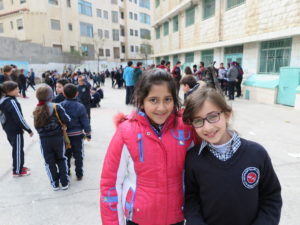 Kaksi palestiinalaistyttöä koulun pihalla Ramallahissa. Taustalla muita oppilaita koulupuvuissa.