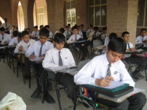 Pakistanilaisia poikia opiskelemassa pulpettien ääressä koulupuvut yllään.