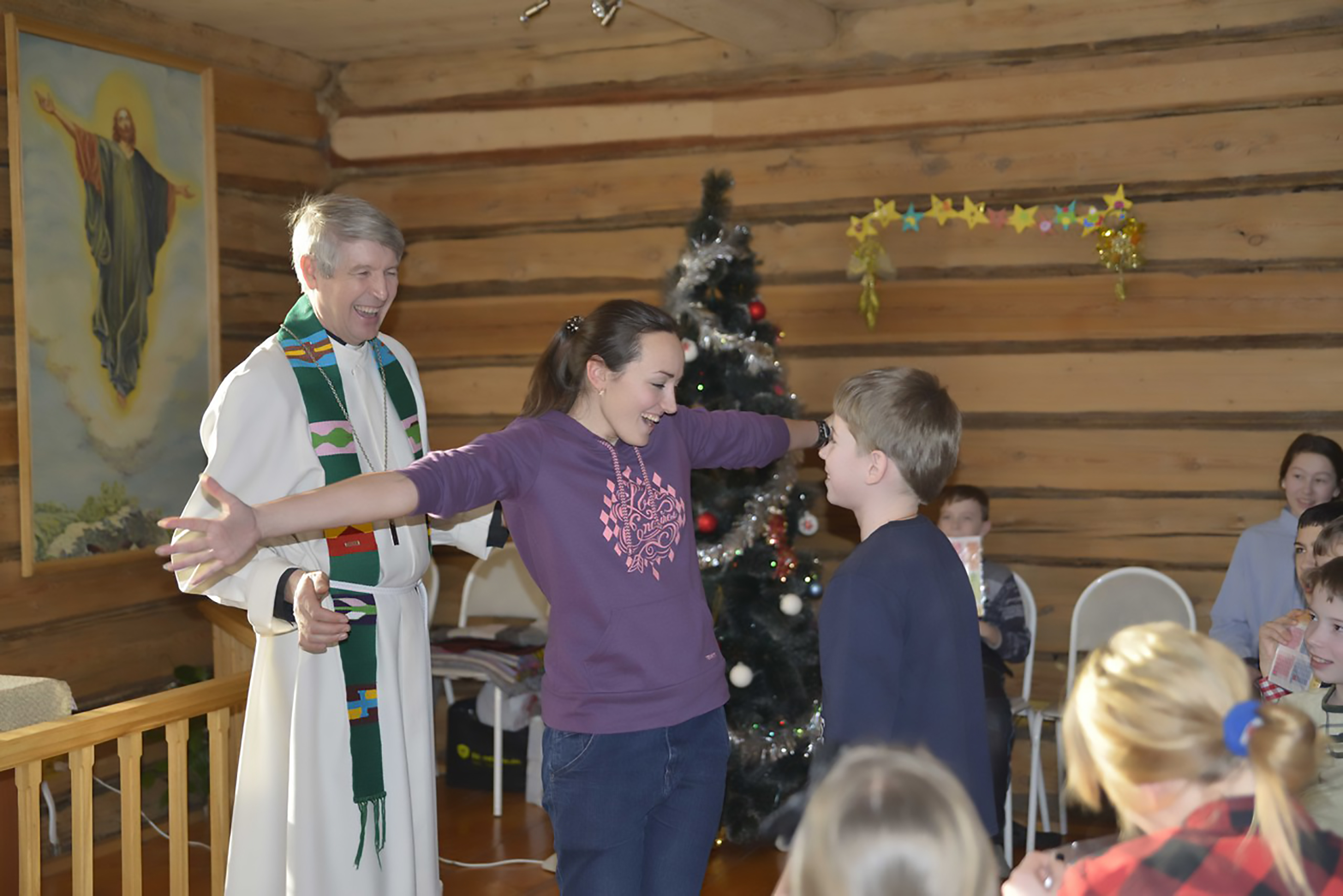 Naurava pappi ja iloinen nuori tyttö, joka levittää käsiään halatakseen nuorempaa poikaa.