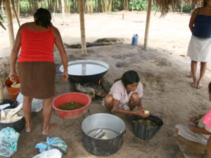 Bild på två människor ur lokalbefolkningen som tillagar mat i kastruller på marken.