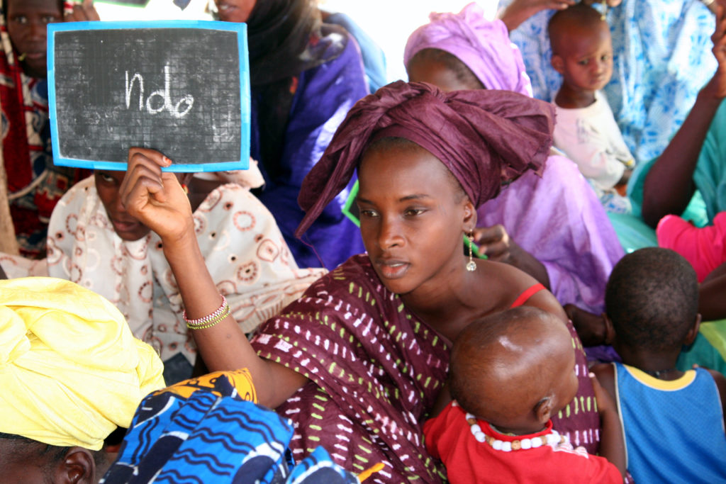 Mauritanialainen nainen opettelee lukemaan lapsi sylissään. Kädessään hänellä on liitutaulu, jossa lukee 