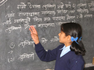 Nepalilainen lapsi tavaa tekstiä liitutaululta.