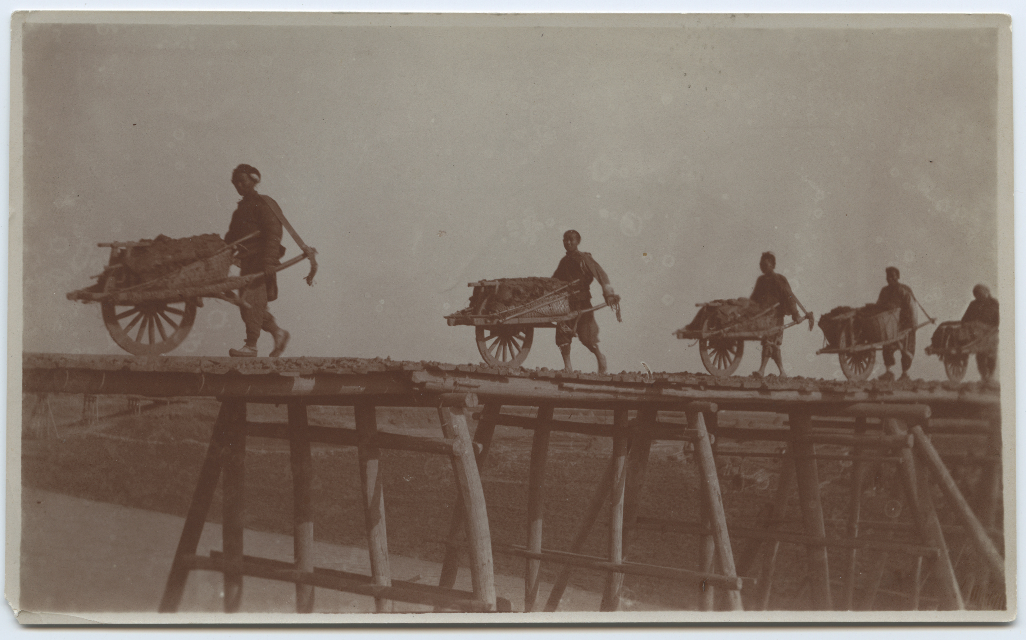 Kiinalaiset työntävät kottikärryjä puusillan yli. Kuva on otettu vuosien 1908 ja 1914 välillä. Kuva Elin Collan