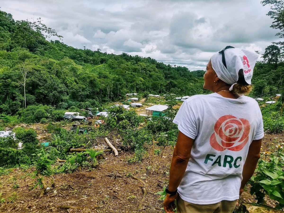 Kuvassa nainen katsoo rehevän pensaikon keskelle rakennettua kylää, naisen T-paidassa lukee Farc.