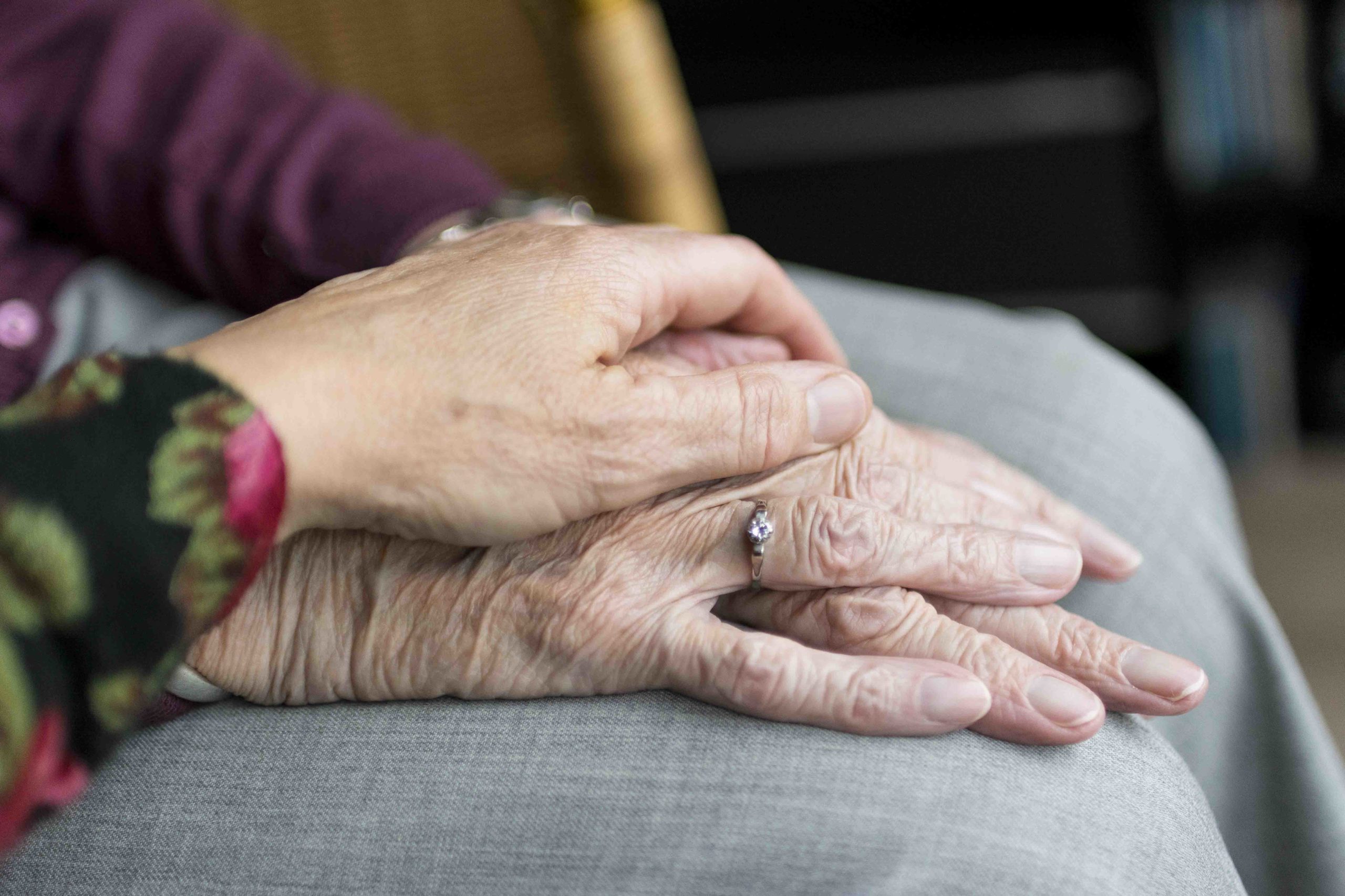 Kuvassa keski-ikäisen naisen kädet lepäävät iäkkään ihmisen ryppyisten käsien päällä.