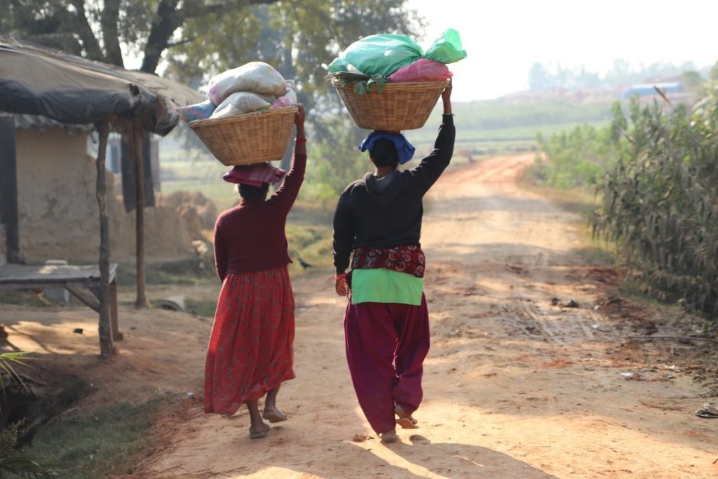 Two people walk on the village road carrying baskets on their head