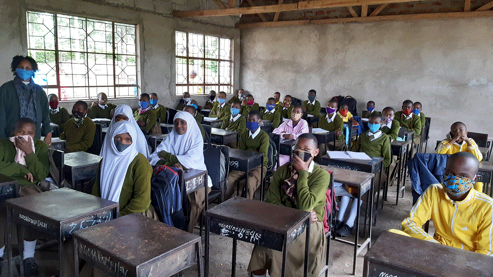 Oppilaat istuvat maskit kasvoilla luokkahuoneessa puupulteissa.