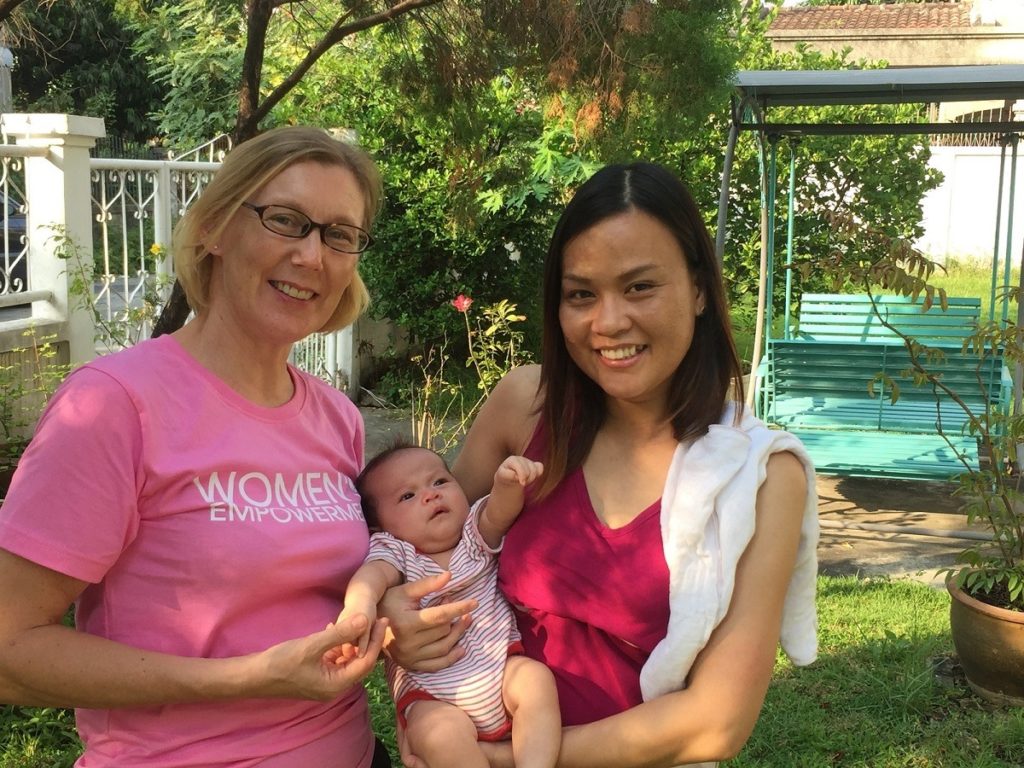 Anja nuoren thaimaalaisen naisen ja hänen vauvansa kanssa ensikodin puutarhassa.