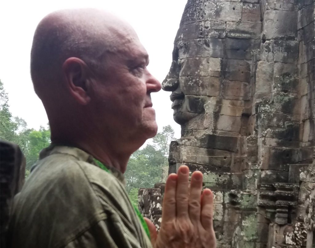 Mies ja kambodzhalainen kivipatsas nenät vastakkain.