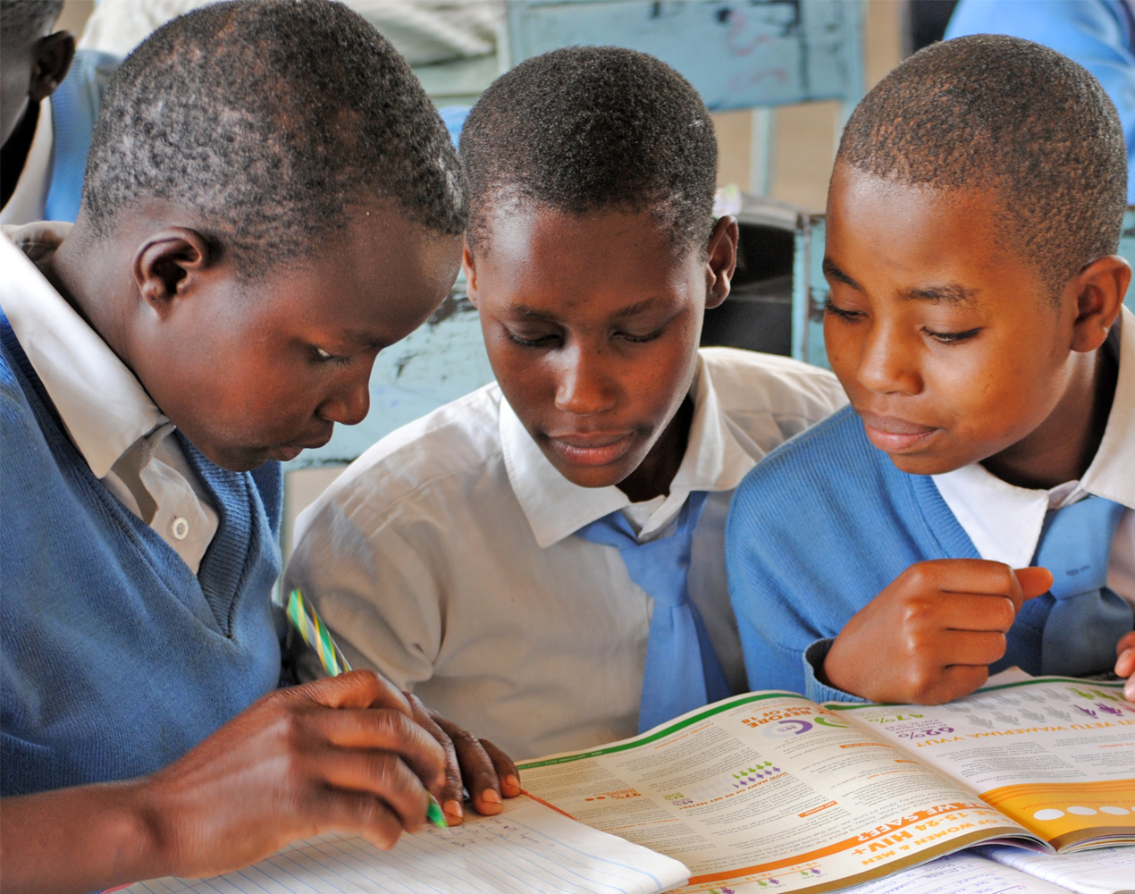 Kolme tansanialaista koululaista päät yhdessä koulukirjan äärelle kumartuneina.