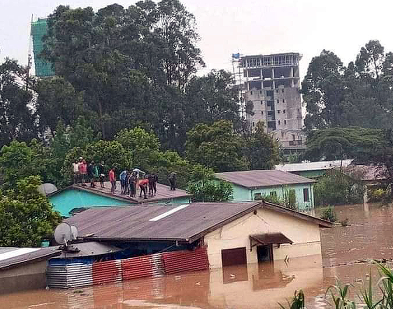 Ihmisiä on paennut tulvaa talon katolle. Vesi ulottuu puoleen väliin talon seinää.