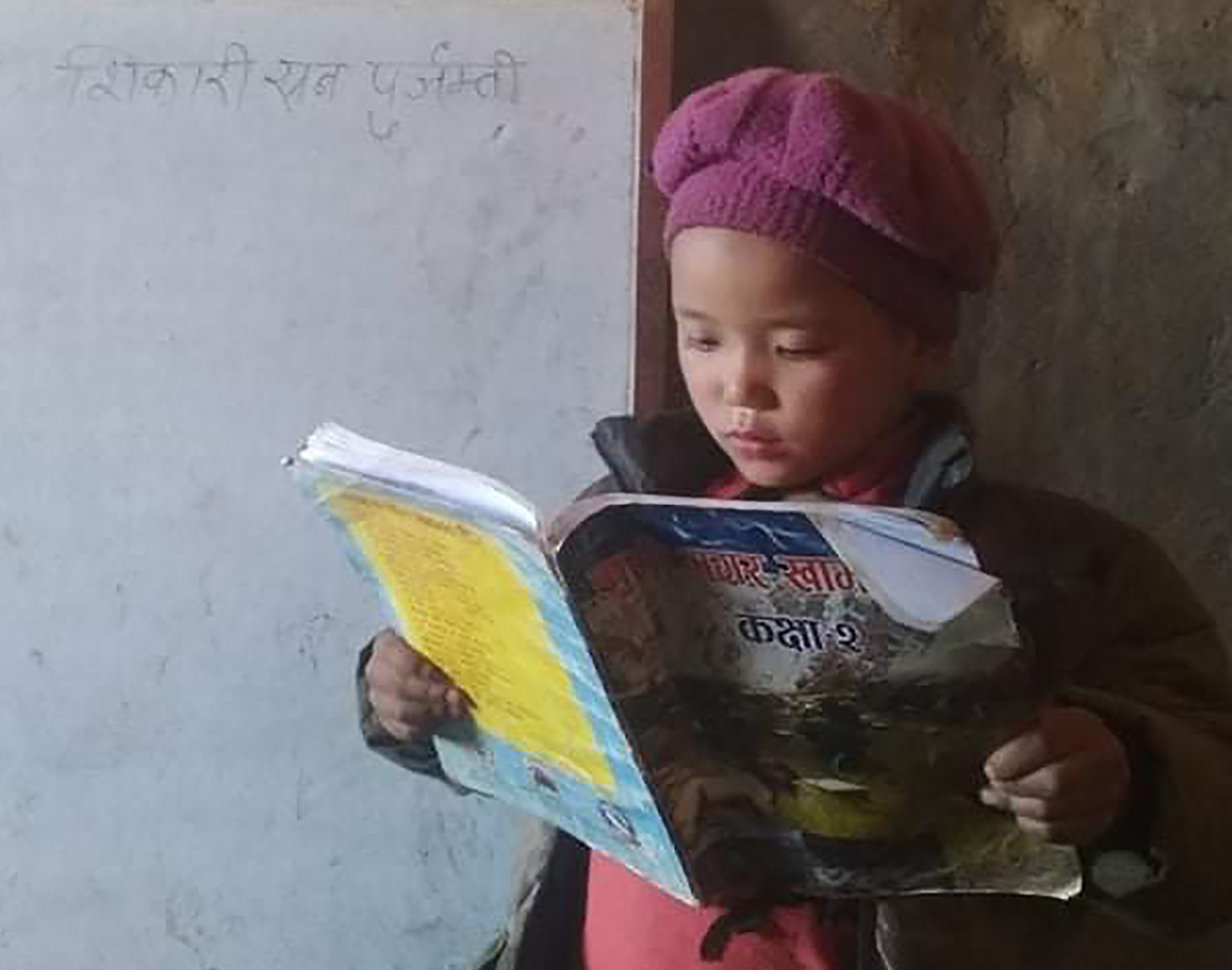 Nepalilaistyttö lukee oppikirjaa taulun edessä.