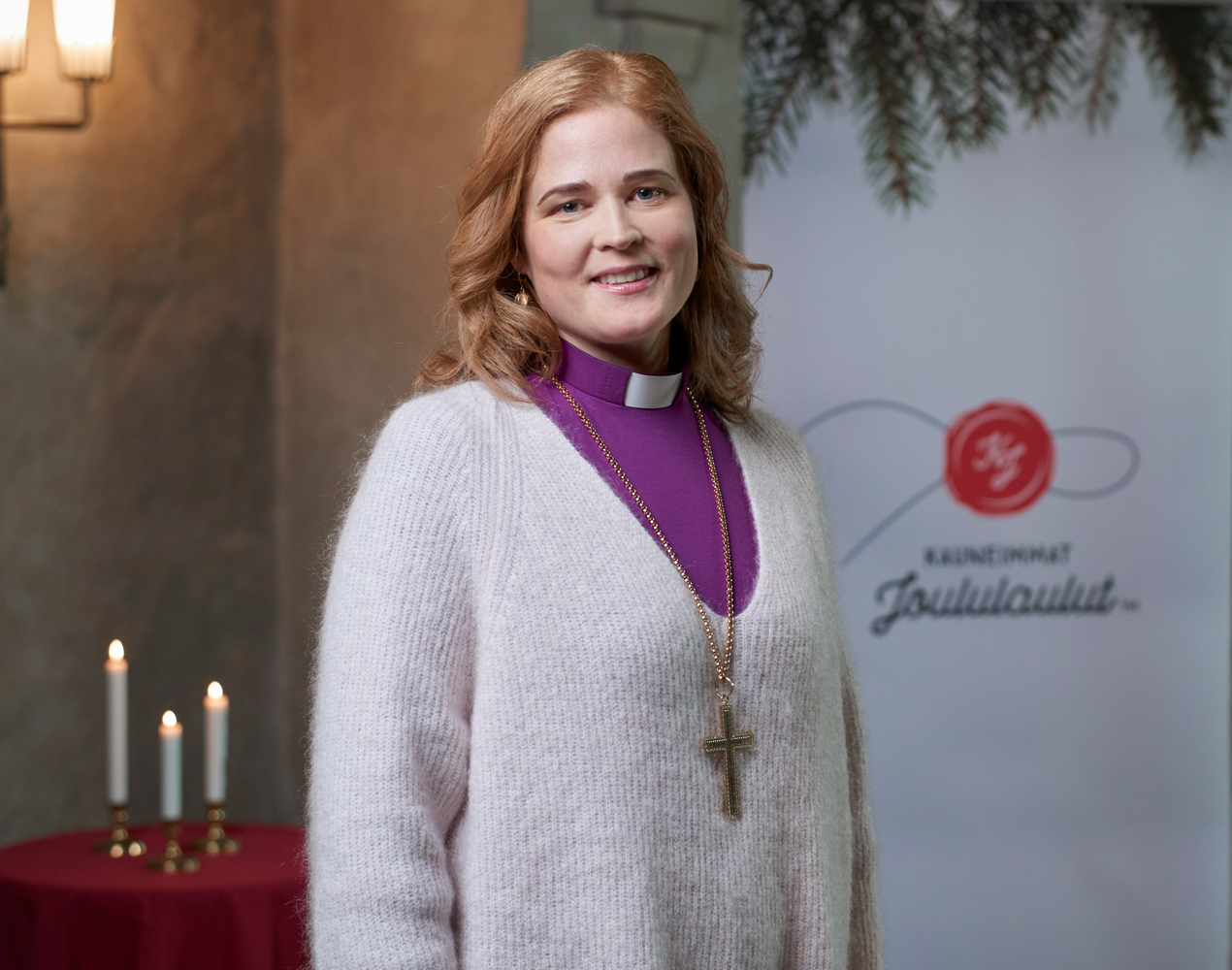 Piispa Mari Leppänen Turun tuomiokirkossa taustalla kolme kynttilää ja Kauneimmat Joululalut -rollup