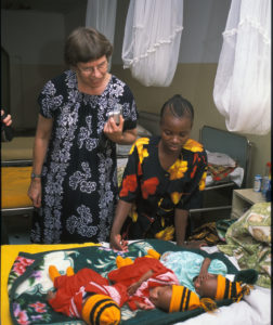 Leena ja tansanialainen äiti ihailevat kolmea värikkäästi puettua vauvaa sängyn päällä.