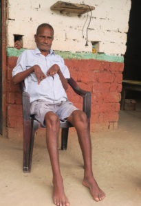 Vammainen nepalilaismies Madan Damai kotitalonsa edustalla tuolilla istuen.