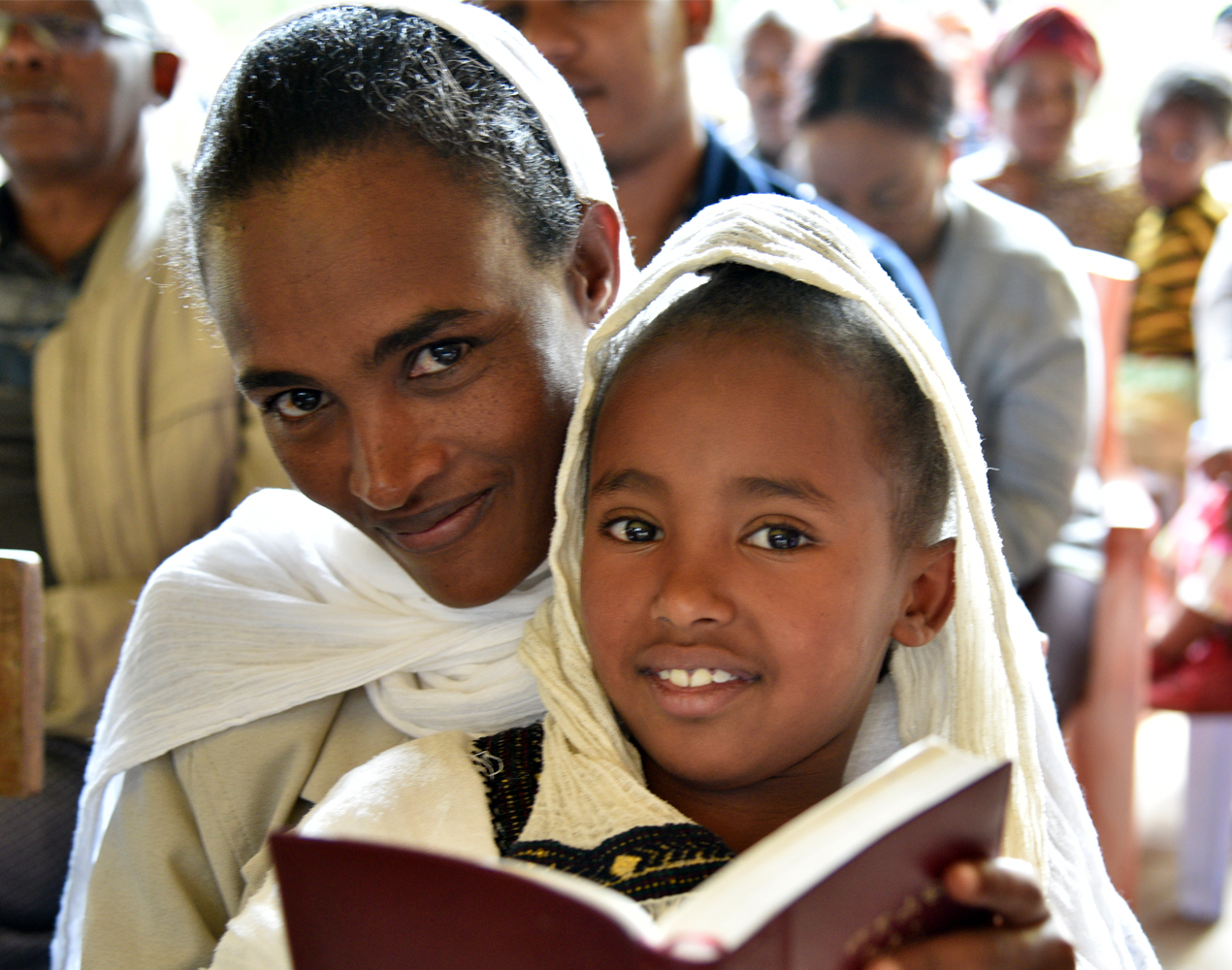 Testamentti-illan mainoksessa etiopialainen äiti tyttärensä kanssa avoin kirja käsissään.