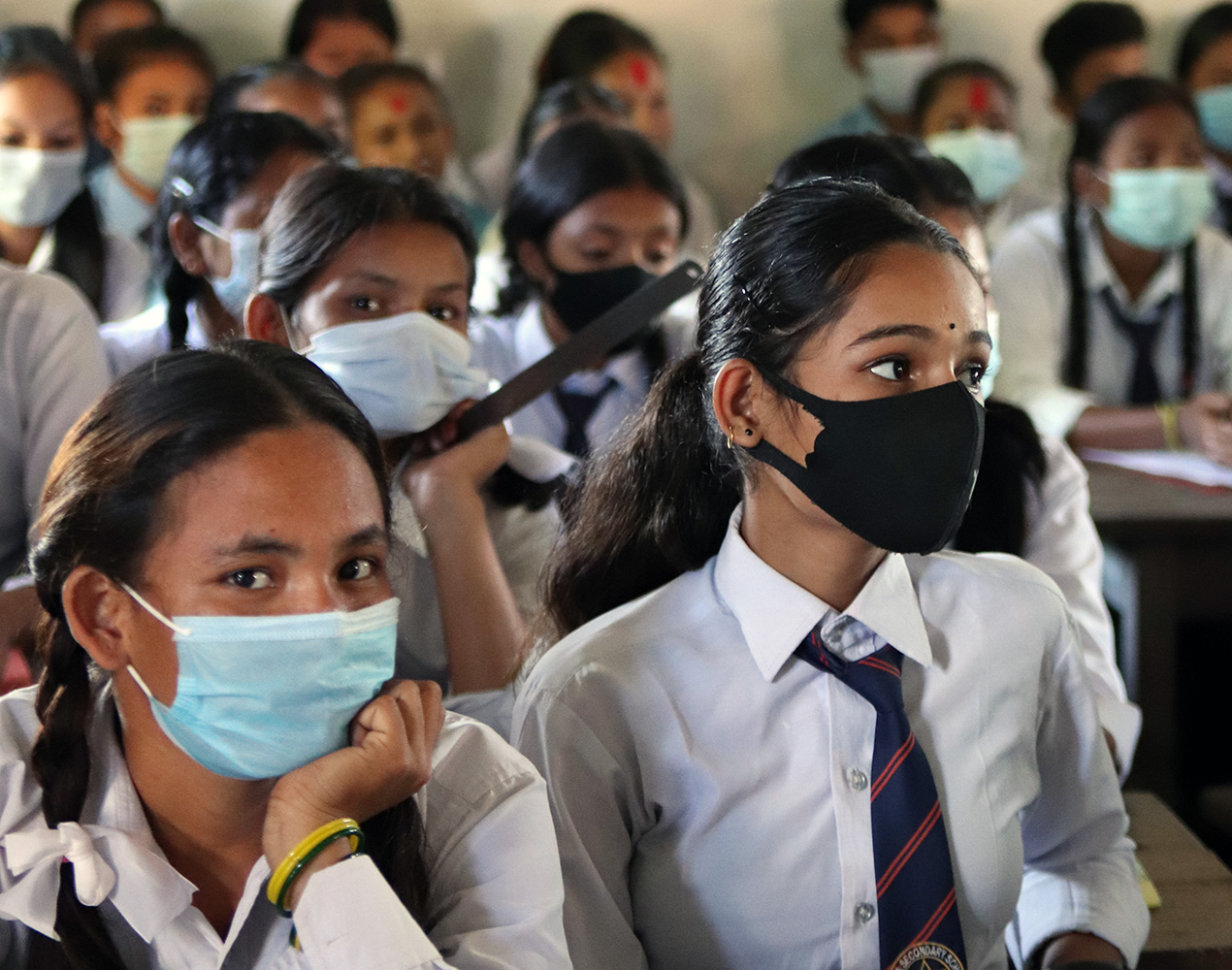 Koulutyttöjä luokassa Nepalissa, kasvomaskit kasvoillaan.