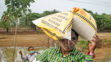 Myanmarilainen nainen kantaa riisisäkkiä päänsä päällä.