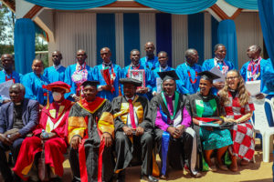 Ryhmäkuvassa edessä istumassa tansanialaisia raamattuopiston opettajia juhlakaavuissaan, takarivissä valmistuneita opiskelijoita sinisissä kaavissa.