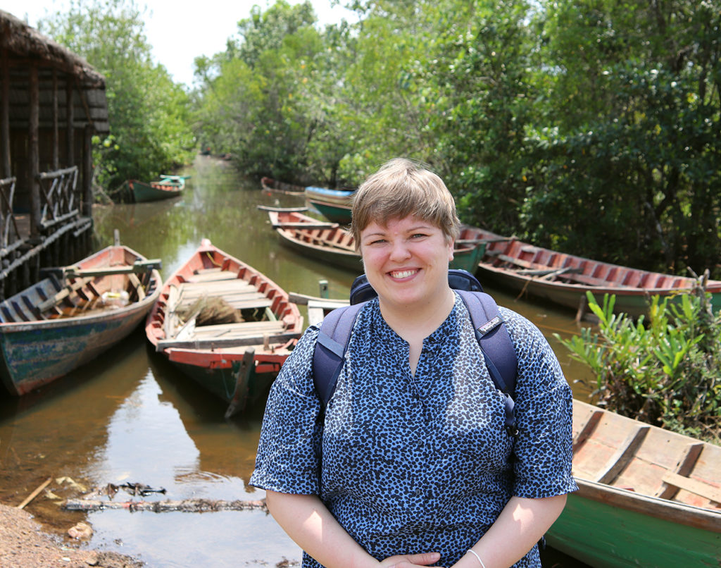 Vapaaehtoinen Johanna Harjunpää seisoo Kambodzassa veneiden ja joen äärellä.