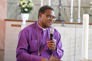 Tansanialainen piispanasuinen mies mikrofoni kädessä alttarin edessä.