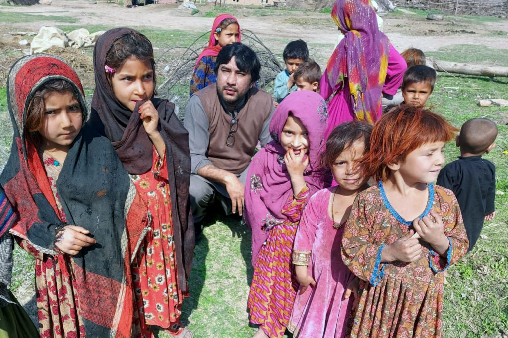 12 afgaanilasta seisoo ulkona värikkäissä vaatteissa. Kuvassa on myös kyykyssä yksi mies.