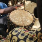 Kuvassa näkyy käsi ja rumpukapula sekä yksi perinteinen afrikkalainen rumpu.