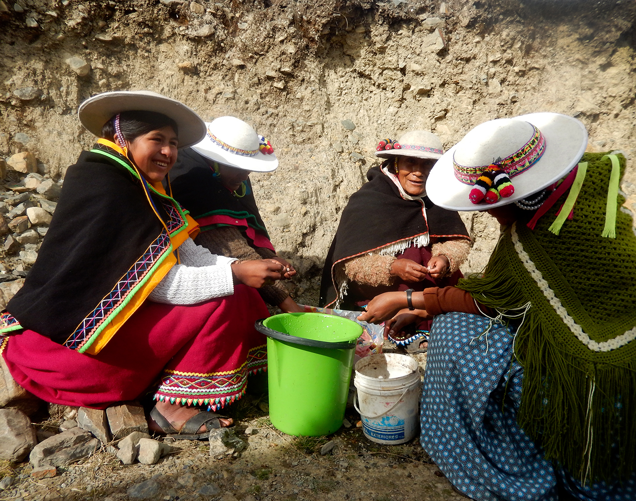 Alkuperäiskansoihin kuuluvia naisia valmistamassa ateriaa. Naisilla on leveälieriset hatut ja lämpimät hartiahuivit.