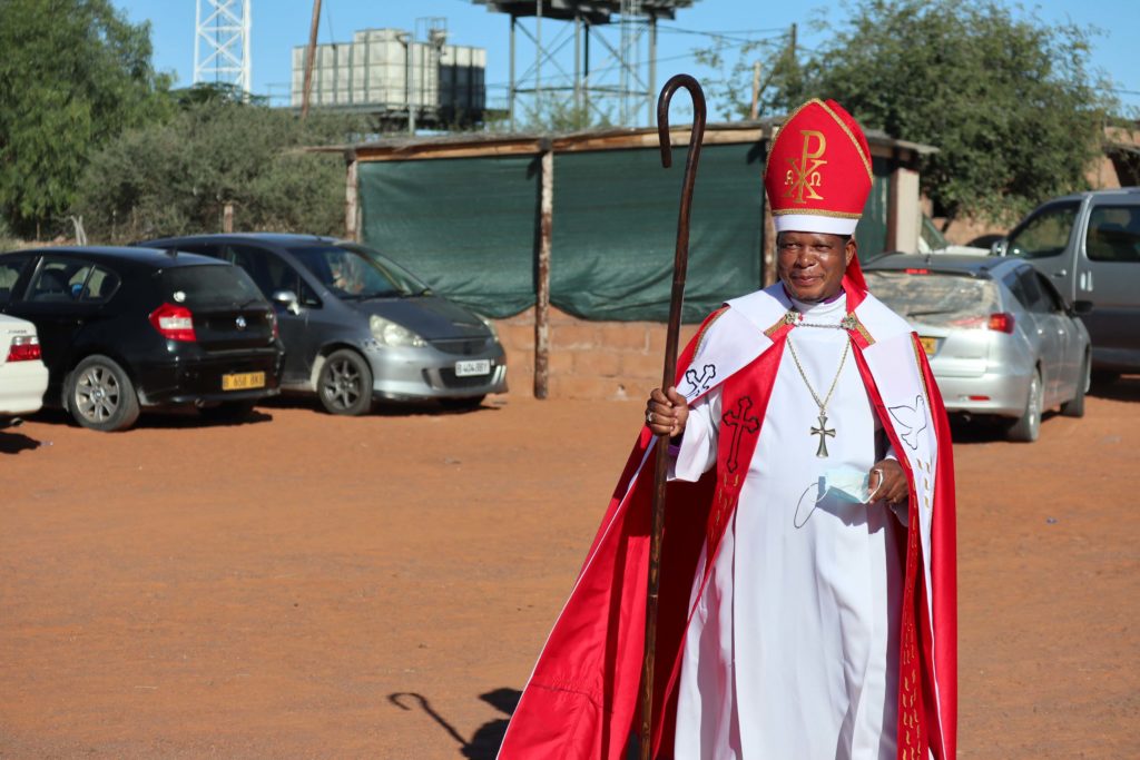 Punaiseen piispan asuun pukeutunut mies kävelee hiekkakentällä.