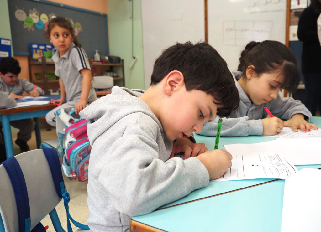 Lapset opiskelevat luokassa. He piirtävät tai kirjoittavat jotain papereihinsa. 
