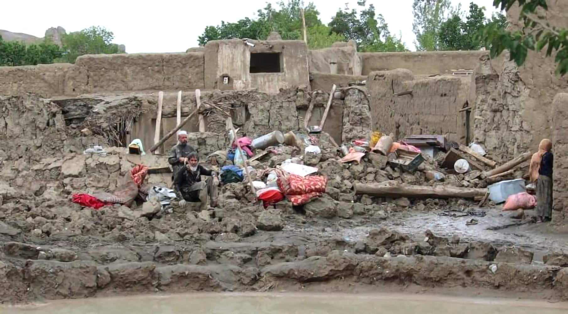 Kuvassa likaisen ruskea joki, jonka rannalla tuhoutuneita rakennuksia ja muutama ihminen.