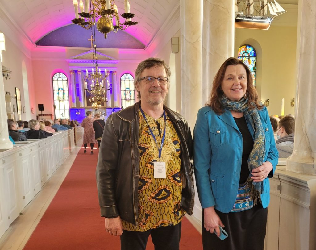 Pekka Simojoki ja Anna-Mari Kaskinen seisovat kirkon käytävällä, taustalla näkyy kirkkosalin etuosaa ja ihmisiä.