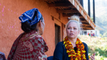 Pippa Laukka keskustelee kameraan selin olevan nepalilaisen naisen kanssa talon edessä.