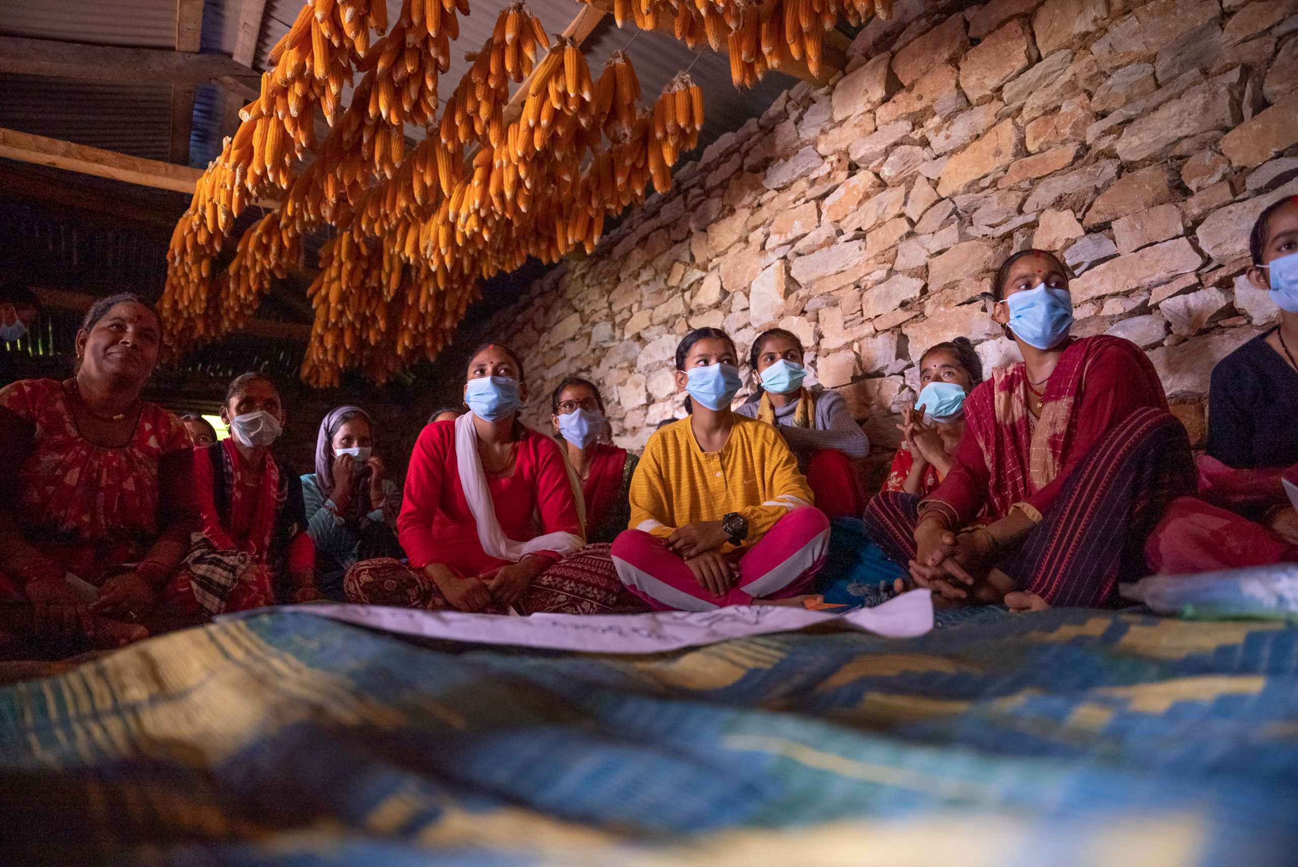 Nepalilaisnaisia istuu lattialla koulutuksessa kasvomaskit kasvoillaan